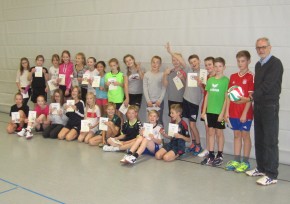 Peter Mehwald (re.) überreicht den neuen Trainings-Volleyball für die Verbundschule Hille, während die erfolgreichen Kinder der 6h stolz ihre Urkunden präsentieren. 